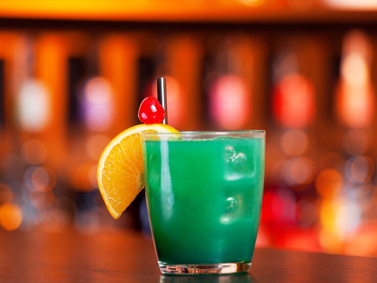 Leuchtend-grüner Cocktail in einem kleinen Trinkglas, dekoriert mit einer Orangenscheibe und einer Cocktailkirsche, 