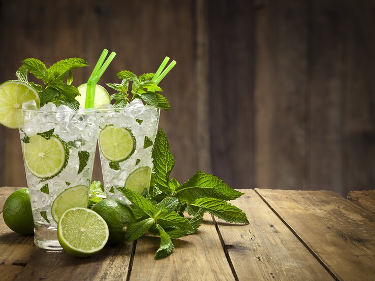 Zwei mit Minze dekorierte Gläser gefüllt mit klassischem Mojito-Cocktail in hölzerner Kulisse. 