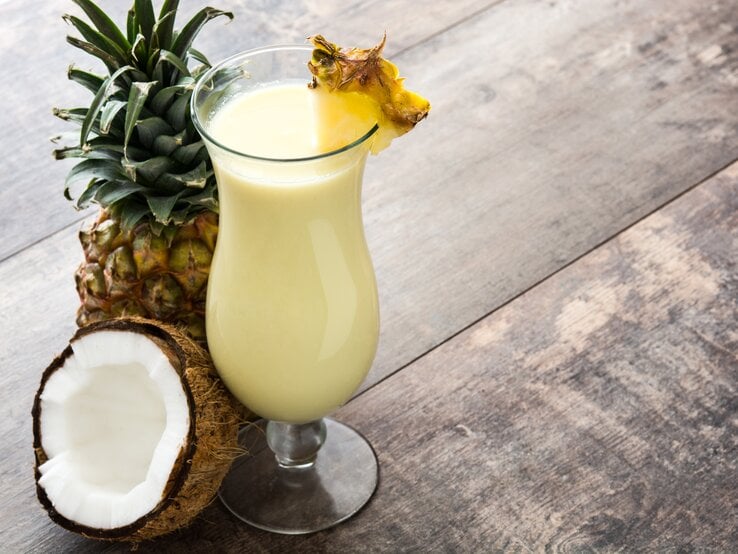 Ein mit Ananas dekoriertes Glas mit cremiger Piña Colada auf Holztisch. 