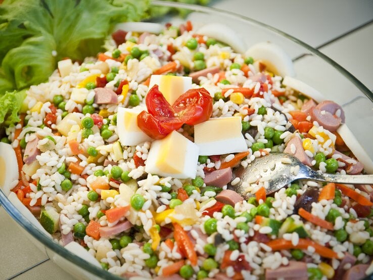 Kunterbunter Reissalat mit Paprika, Würstchen, gekochtem Ei und Erbsen in Glasschüssel. 
