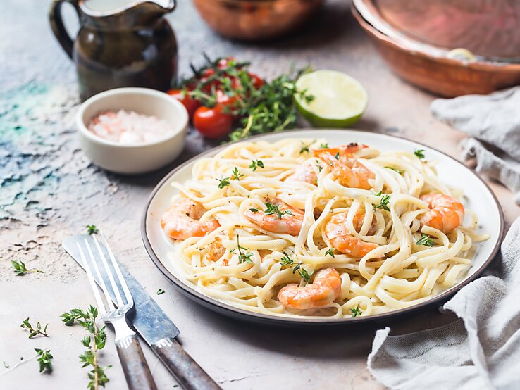 Ein Teller mit frisch zubereiteten Pasta, garniert mit saftigen, rosa Garnelen und fein gehackten Kräutern, serviert auf einem rustikalen Küchentisch.