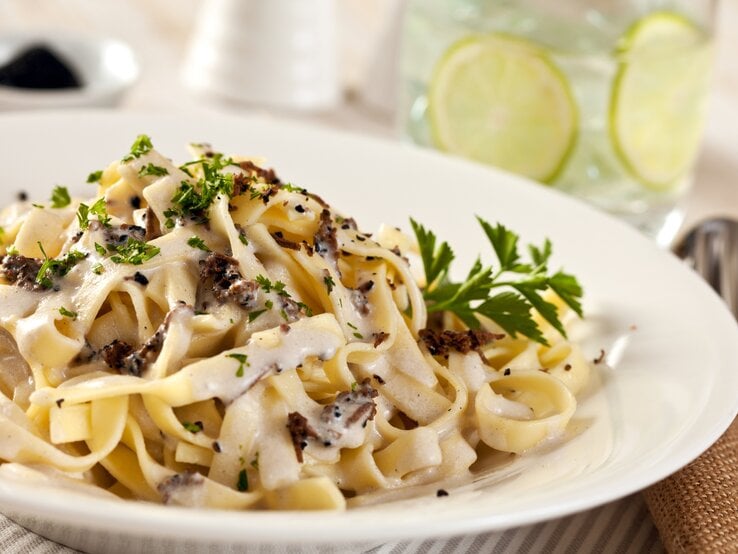 Ein weißer Teller, darauf Pasta mit Trüffeln, Parmesan und cremiger Soße. 