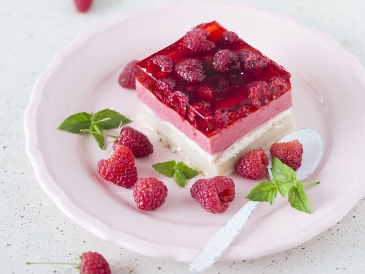 Ein Stück vom Himbeerkuchen auf einem hellen Teller weißem Untergrund.