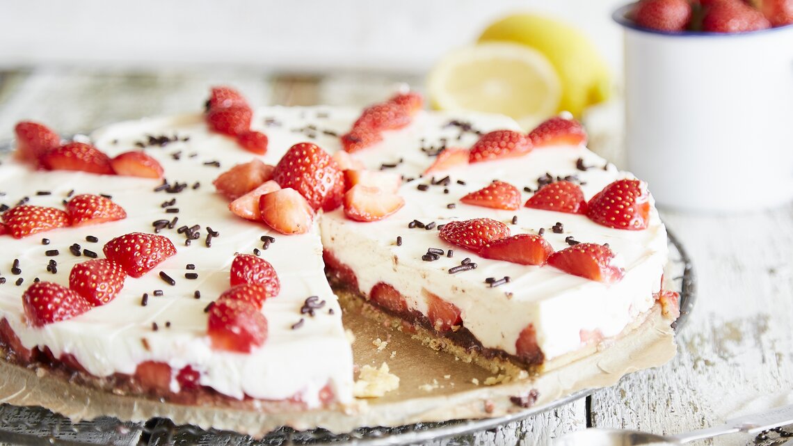 Ansprechende Erdbeertorte mit weißer Creme und dunklen Schokoladenstreuseln, präsentiert auf Holzuntergrund.