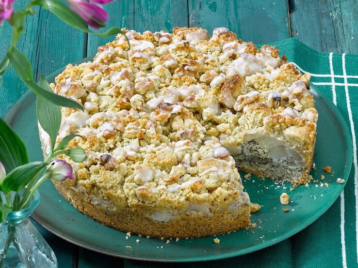 Der Mohnkuchen auf einem türkisenen Teller und türkisen Holztisch. Alles von der Seite fotografiert.