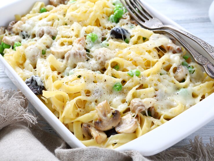 Ein Auflaufgericht mit cremigen Bandnudeln, gemischt mit grünen Erbsen und geschnittenen Champignons, großzügig überzogen mit geschmolzenem Käse. 