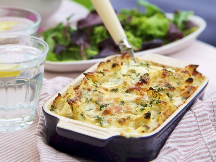 Nudel-Schinken-Auflauf in einer Form / Hintergrund grüner Salat / 