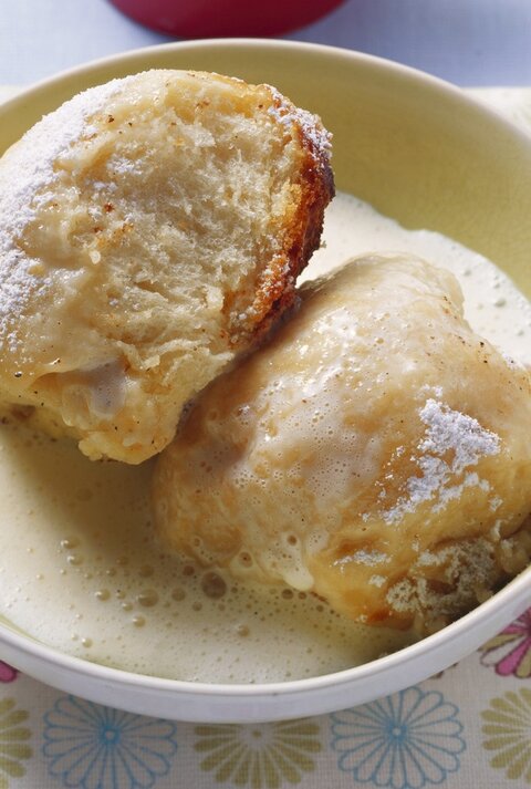 Zwei Dampfnudeln mit Vanillesoße in einer hohen, runden Schale aus Porzellan / Untergrund quadratische papierserviette auf glattem Boden