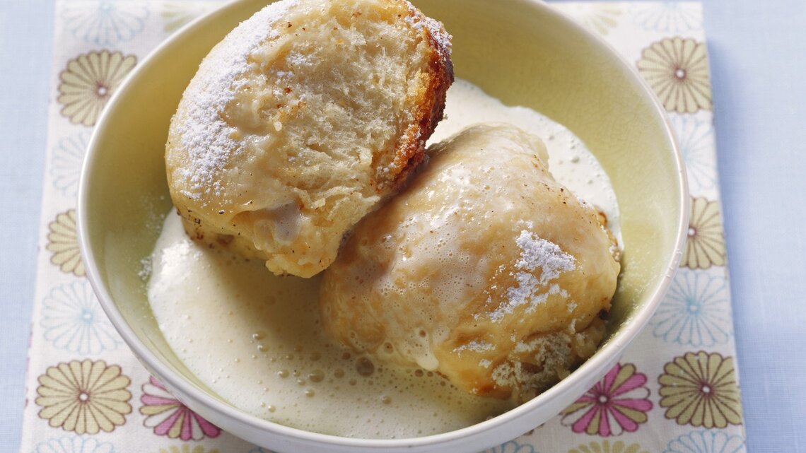 Zwei Dampfnudeln mit Vanillesoße in einer hohen, runden Schale aus Porzellan / Untergrund quadratische papierserviette auf glattem Boden