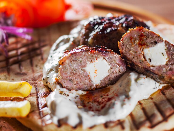 Angeschnittenes, griechisches Hacksteak "Bifteki" mit Feta-Füllung. Darunter ein Fladenbrot, daneben Pommes Frites. 