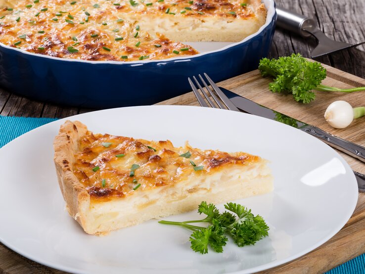 Ein Stück Käse-Quiche auf Teller in rustikalem Ambiente.