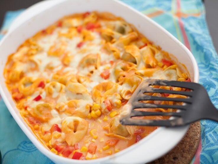 Weiße Auflaufform gefüllt mit Tortellini, Mais und cremiger Tomatensoße. 