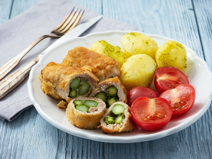 Schnitzel gefüllt mit Spargel zu Dill-Kartoffeln und Tomaten auf weißem Teller. 