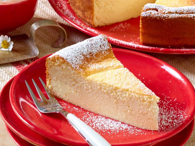 Ein Stück Käsekuchen auf einem roten Teller und hellem Holztisch. Alles von schräg oben fotografiert.