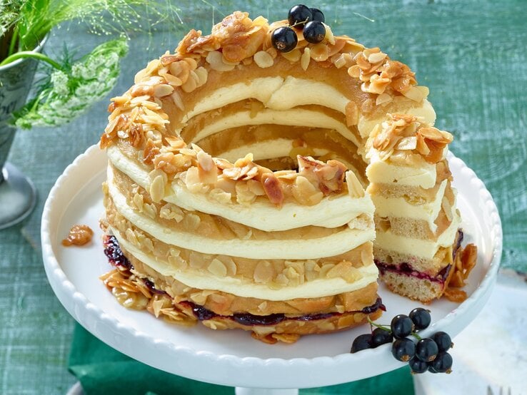 Der Johannisbeer-Bienenstichkranz auf einer weißen Etagere mit dunkelgrünem Untergrund. Alles von schräg oben fotografiert.