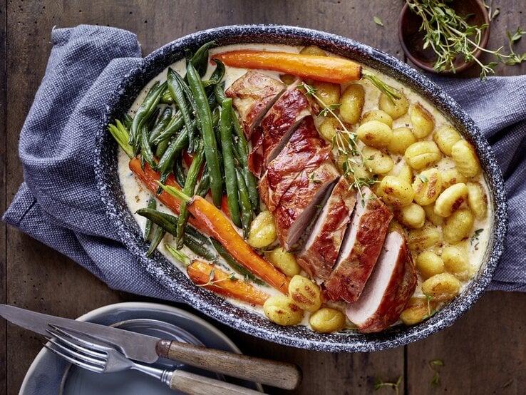 In Rahmsoße gebackenes Schweinefilet mit Gnocchi, glasierten Möhren und grünen Bohnen in rustikaler Auflaufform.