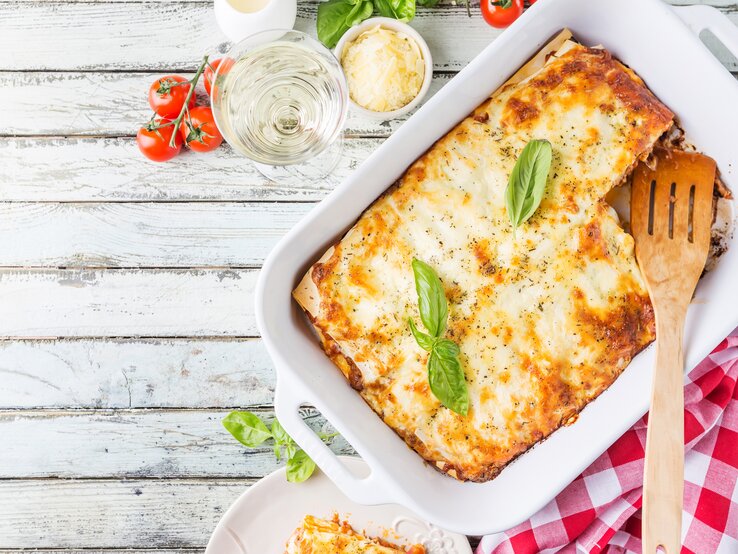 Die Lasagne auf einem hellen Holztisch von oben in der Auflaufform fotografiert.