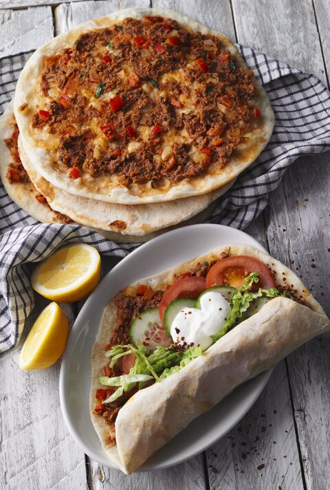 Draufsicht: Vier türkische Pizza Lahmacun. Drei nur mit Hackfleisch, eine mit Tomaten, Gurkenscheiben, Salat und Joghurtsauce