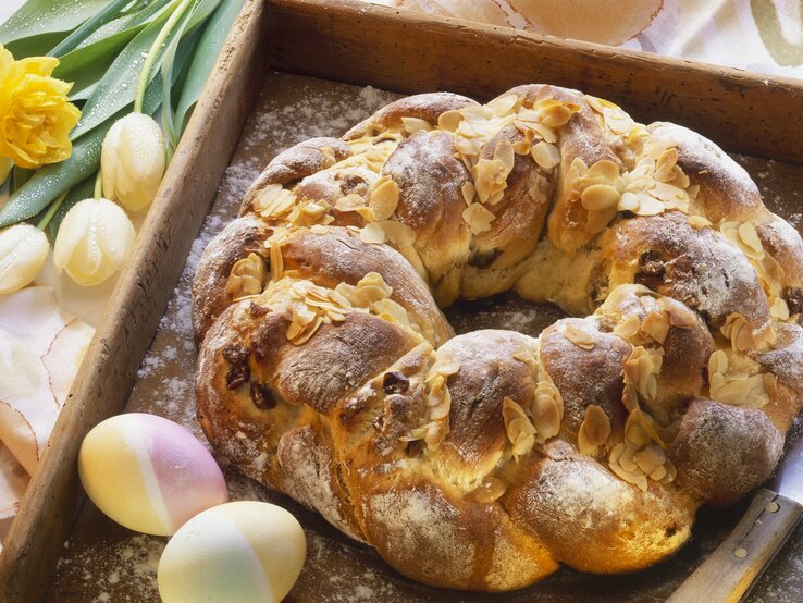 Der Osterkranz auf einem Holzbrett mit Oster-Deko im Hintergrund.