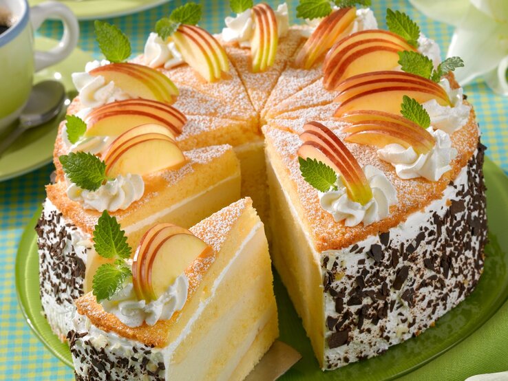Die Apfelcreme-Schichttorte auf einem Tisch mit hellgrüner Tischdecke von schräg oben fotografiert.