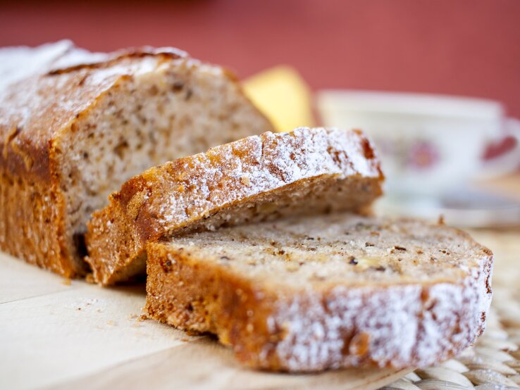 Bananen-Kastenkuchen mit Schokoflakes und mit Puderzucker bestreut auf Holzbrett. 