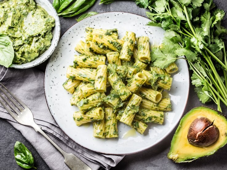 Avocadopesto Weißer teller, darauf angerichtet Penne mit einem cremigen Avocado-Pesto. Die Zutaten sind drumherum verteilt.