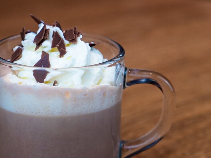 Ein Glas heiße Schokolade mit Sahne und Schokoladenstreuseln obendrauf, serviert auf einem Holztisch, ein gemütliches Getränk für kalte Tage.