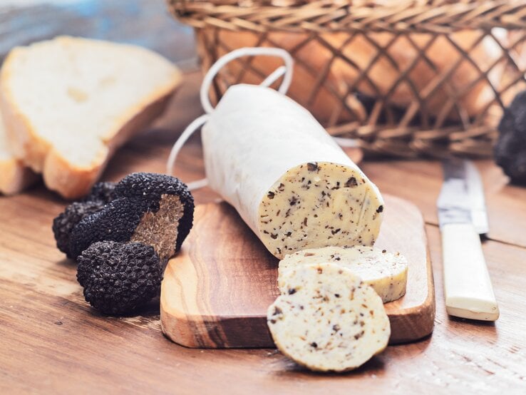 Angeschnittene Rolle Trüffelbutter arrangiert auf einem Holzbrett. 