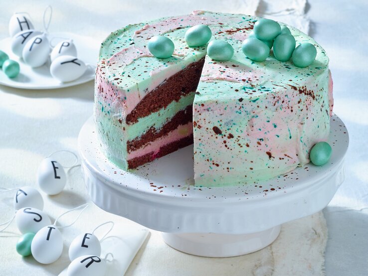 Waldmeister-Himbeer-Torte: Ostertorte mit grünlicher Creme und Schokoeiern auf einem weißen Servierteller.