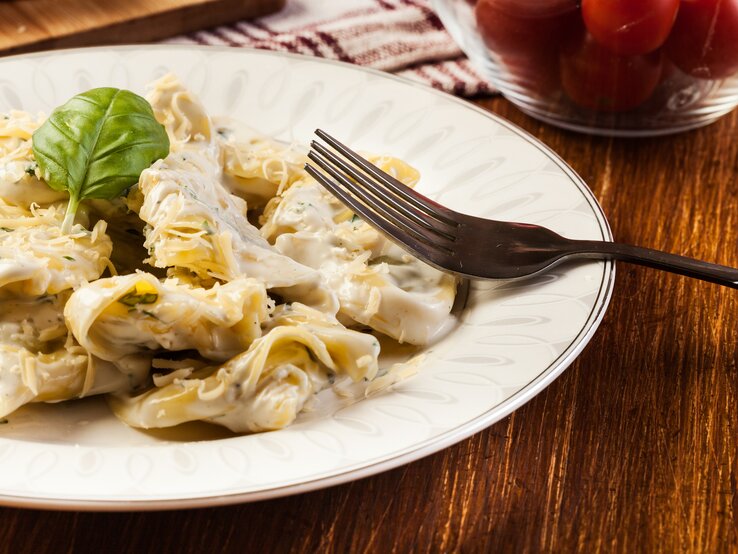 Tortellini mit Käse in cremiger Soße auf weißem Teller 