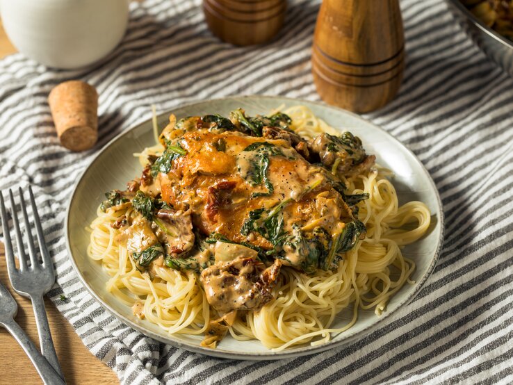 Toskanische Hähnchenpfanne mit Spaghetti, Spinat und getrockneten Tomaten auf weißem Teller. 