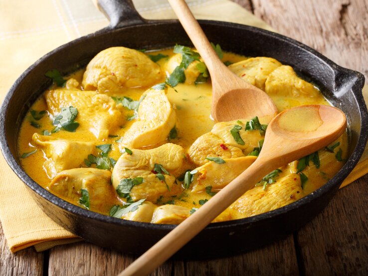 Gusseiserne Pfanne mit Hähnchen-Curry auf hölzernem Untergrund. 