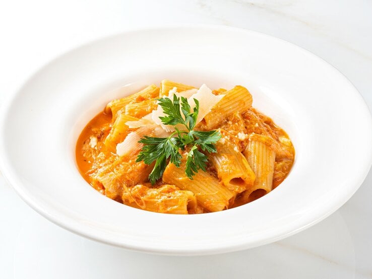 Pasta in Creme-fraiche-Soße in weißem Teller auf weißem Untergrund mit Petersilie. Draufsicht.