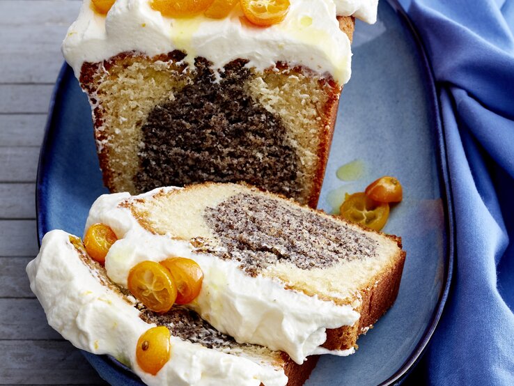 Mohn-Joghurt-Kuchen auf einem blauen Teller vor blauen Hintergrund. Rechts ein blaues Tuch. 