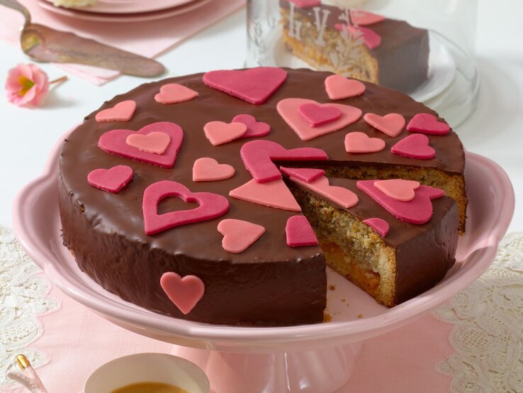 Ansicht einer Haselnusstorte mit dunklem Schokoladenüberzug und roten Marzipanherzen auf einem Kuchenteller