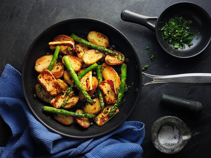 Spargel-Halloumi-Pfanne mit Kartoffeln und leichtem Dressing Spargel-Halloumi-Pfanne mit Kartoffeln in gusseiserner Pfanne auf dunklem Untergrund.