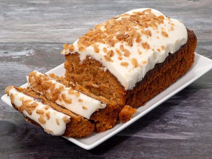 Karottenkuchen mit Creme drapiert auf weißer Platte auf grauem Holz.