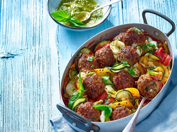 Draufsicht: ein Ratatouille-Hackbällchen-Pfanne in einer Form. Daneben eine runde Schale mit einer Sauce.