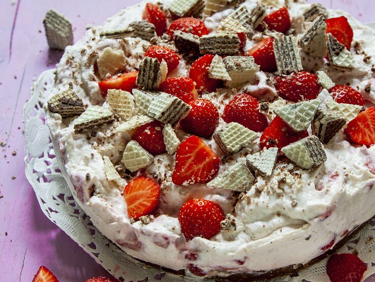 Die Erdbeer-Manner-Torte auf einem violetten Holztisch von schräg oben fotografiert.