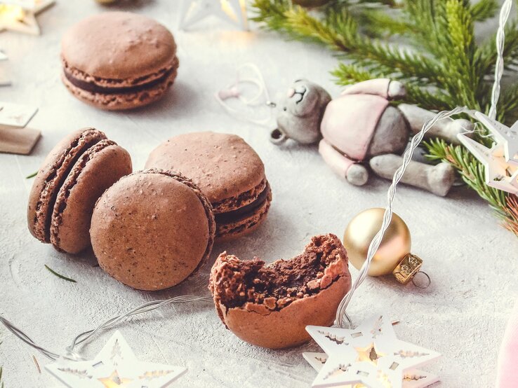 Weihnachtliche Schokoladen-Macarons mit Haselnüssen und Tonkabohne auf einem grauen Tisch mit weihnachtlicher Deko.
