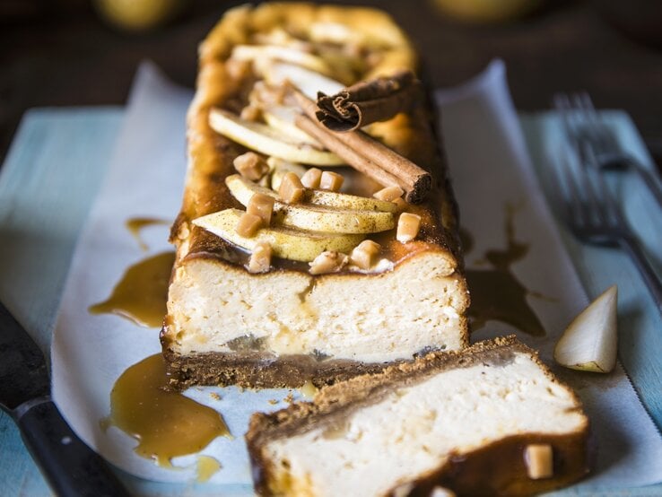 Der Toffee-Birnen-Käsekuchen angeschnitten auf einer bläulichen Serviette von vorne fotografiert.