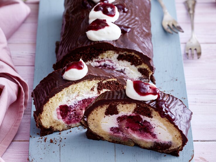 Donauwellen-Rolle angeschnitten auf einem länglichen Brett von schräg oben fotografiert. Rechts liegen zwei Gabeln, links ein Geschirrtuch.