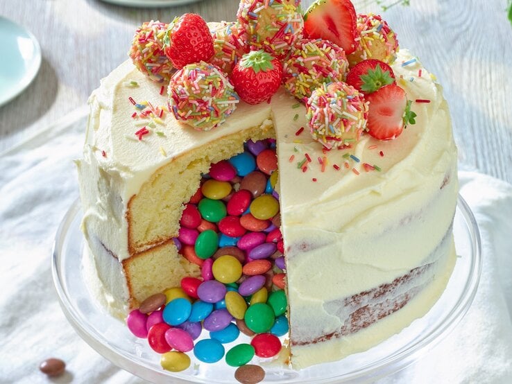 Piñata-Torte mit Erdbeeren auf einem Tortenteller vor weißem Hintergrund. 