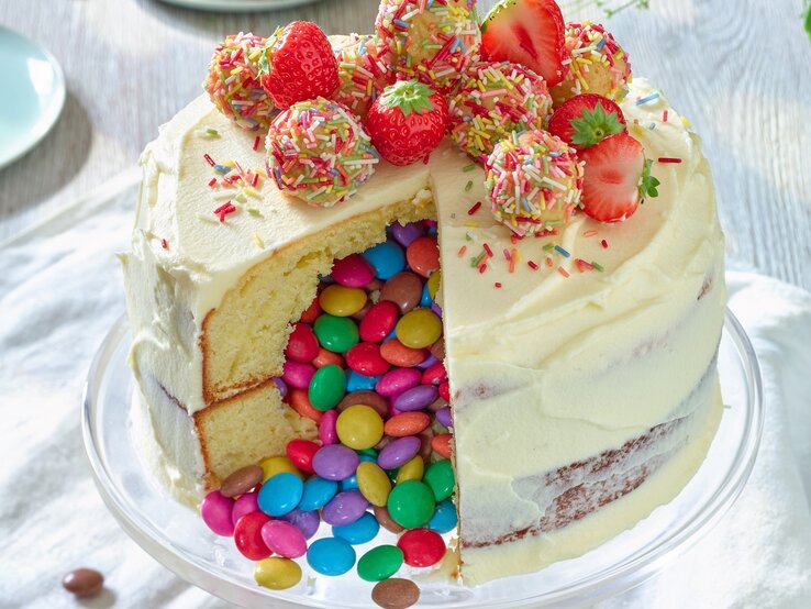 Kreative und kunterbunte Piñata-Torte mit Erdbeeren zum Nachbacken. Piñata-Torte mit Erdbeeren auf einem Tortenteller vor weißem Hintergrund.