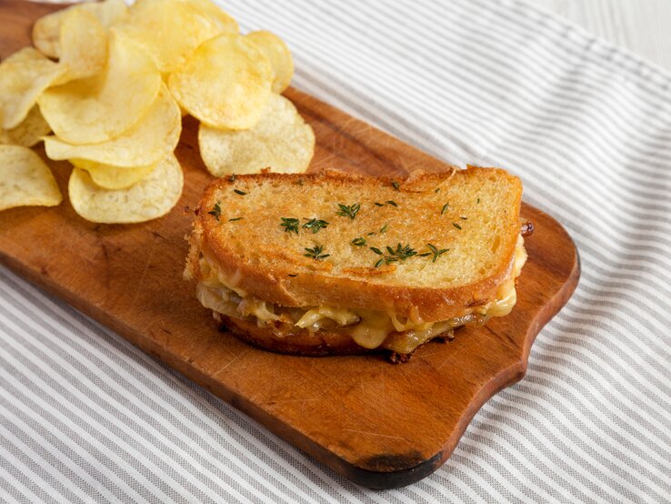 Französisches Käsesandwich mit geschmelzten Zwiebeln und Chips auf Holzplatte auf Tuch. Draufsicht.