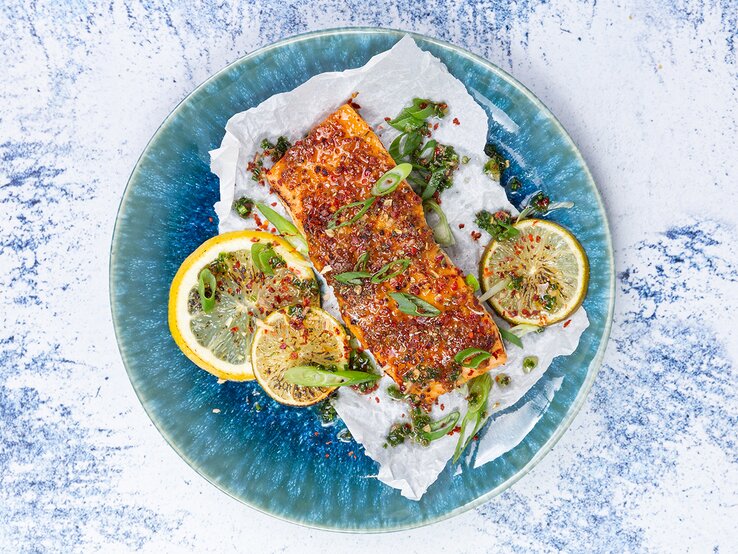 Karamellisierter Lachs mit Koblauchreis auf einem blauen Teller auf weiß-blauem Hintergrund.