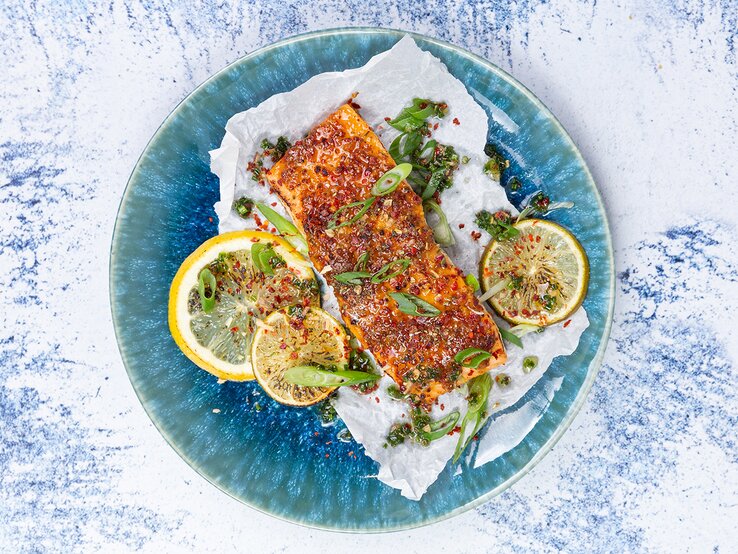 Wenn du auf der Suche nach einem Gericht bist, das Freunde und Familie zum Staunen bringt, musst du karamellisierter Lachs mit Knoblauchreis zubereiten! Karamellisierter Lachs mit Koblauchreis auf einem blauen Teller auf weiß-blauem Hintergrund.