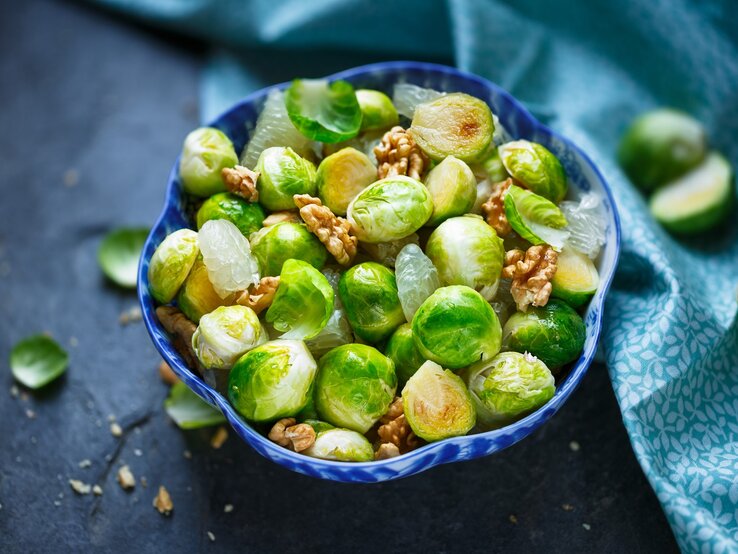 Gerösteter Rosenkohlsalat mit Walnuss, Pomelo und Honig-Dressing in blauer Schüssel auf blauem Untergrund. Draufsicht.