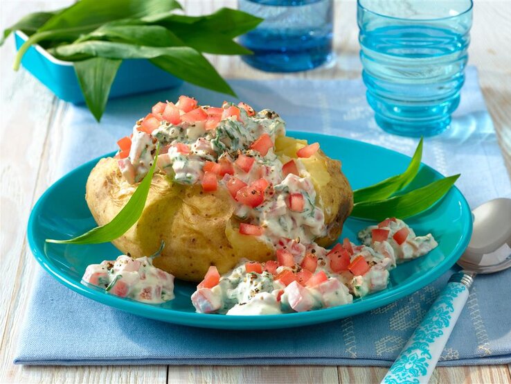 Große aufgeschnittene Kartoffel mit Tomaten-Bärlauch-Quark auf blauem Teller