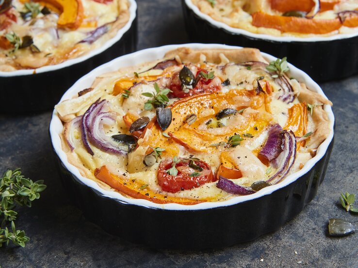 Die Kürbis-Quiche mit roten Zwiebeln in einer schwarzen Auflaufform gebacken.